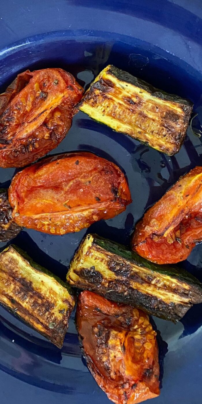 Roasted zucchini and cherry tomatoes glistening with herbs, served on a tray beside lemon chicken