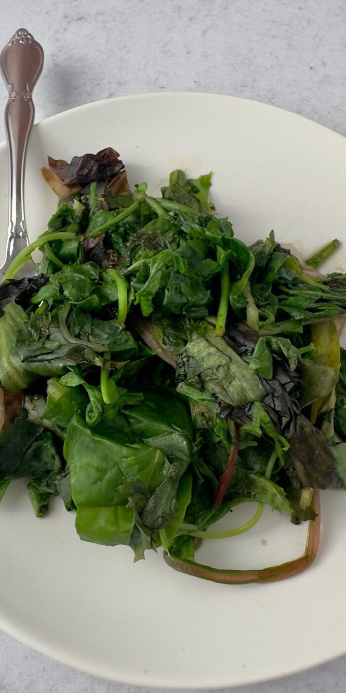 Mixed saut&eacute;ed greens glistening in a skillet, served as a side dish with lemon pepper chicken.