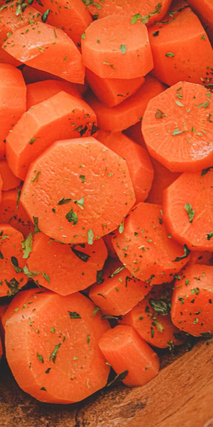 Bright orange steamed carrots glistening in a white bowl, served as a side for lemon pepper chicken.