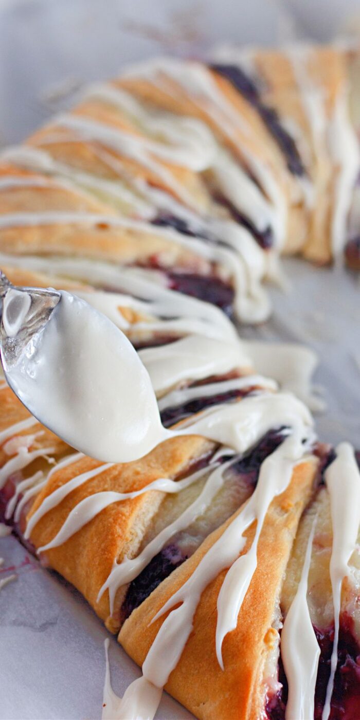 Close-up of a raspberry cream cheese crescent dessert ring with drizzle on top.