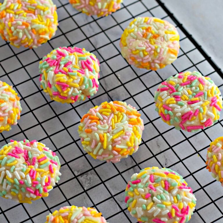 A batch of golden sprinkle cookies made with cream cheese, stacked on a plate and ready to serve.