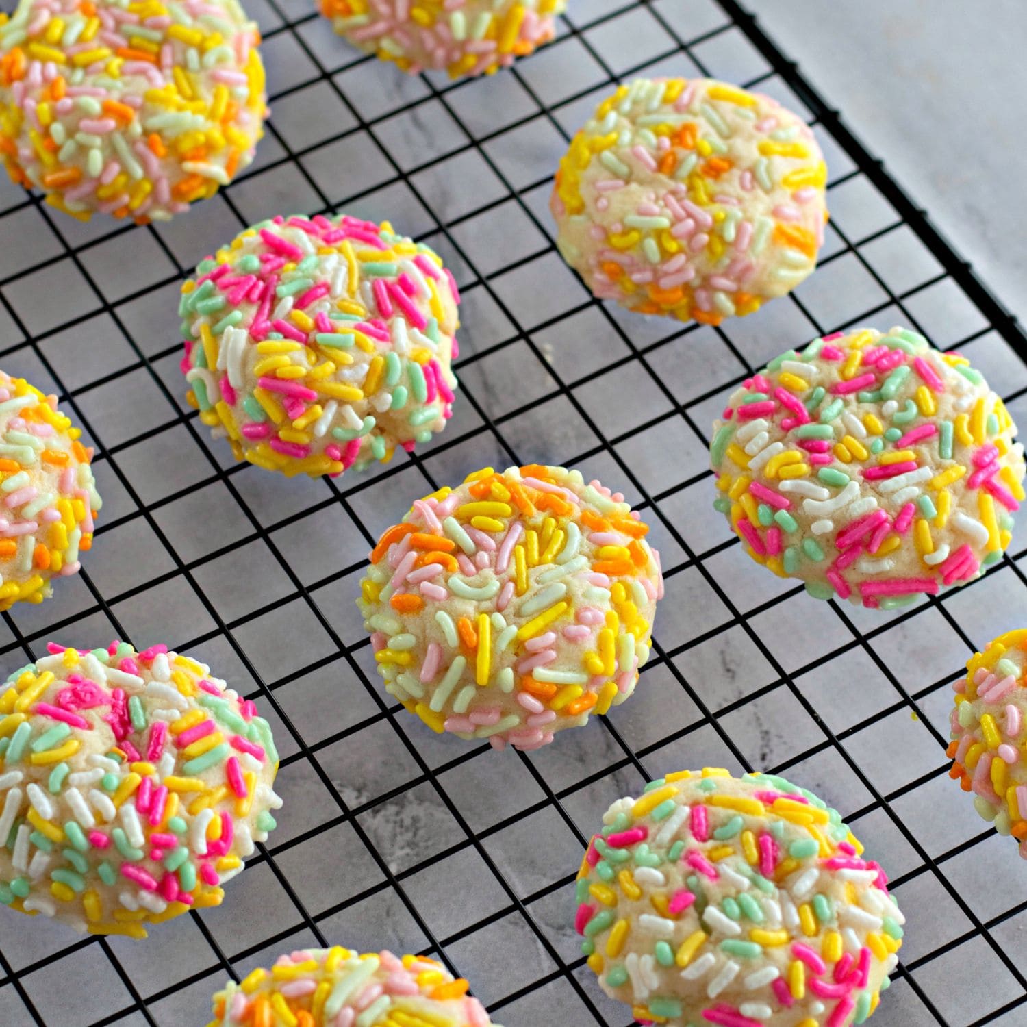 A batch of golden sprinkle cookies made with cream cheese, stacked on a plate and ready to serve.