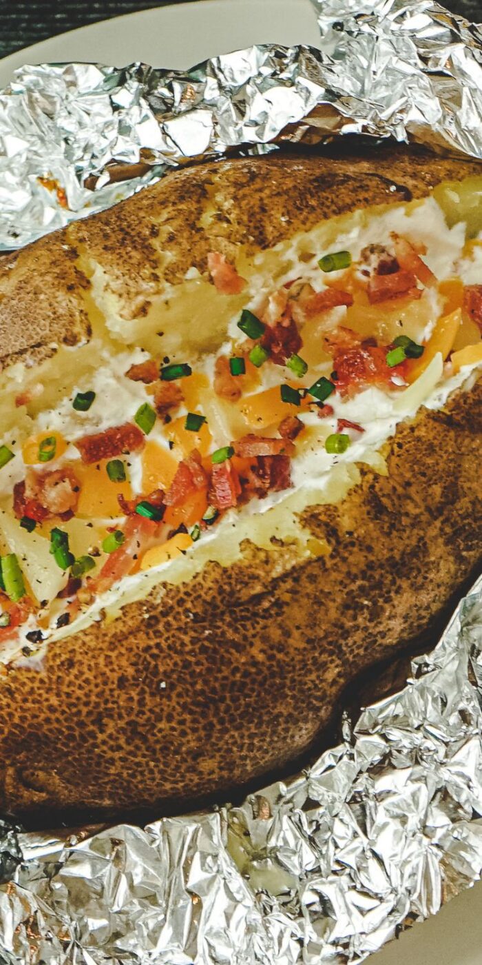 A crispy, golden-brown baked potato split open, revealing a fluffy interior topped with butter and herbs.
