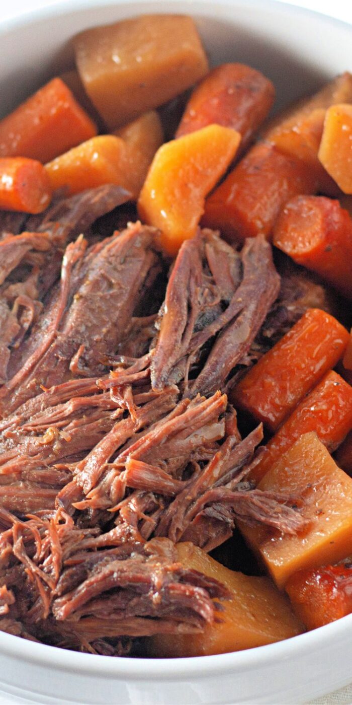 Slow cooker beef roast served with vegetables on a white platter, showcasing a tender, fall-apart texture and hearty flavors