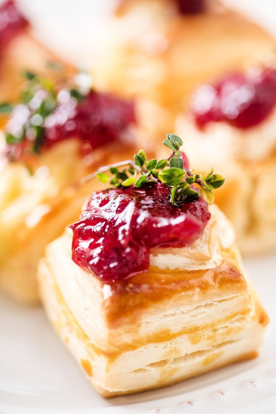 Golden-brown puff pastry cups filled with melted brie and cranberry sauce, garnished with rosemary.
