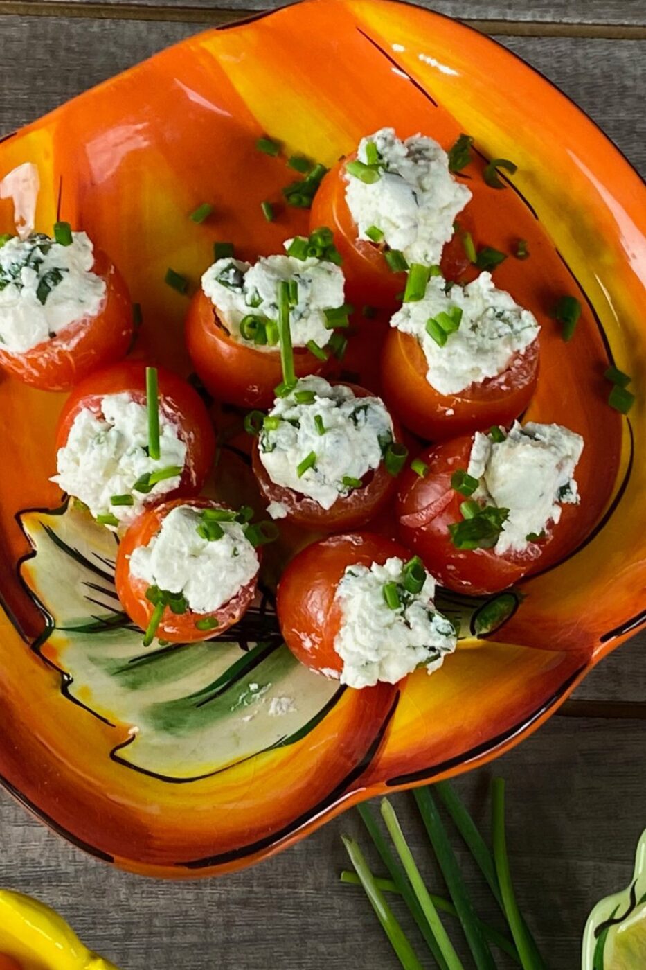 A platter of red cherry tomatoes stuffed with creamy white goat cheese and green herbs.