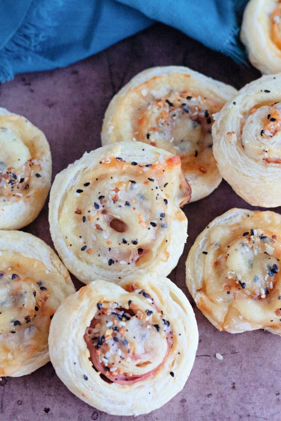 Golden-brown puff pastry pinwheels filled with ham and melted cheese, cut into slices on a serving board.