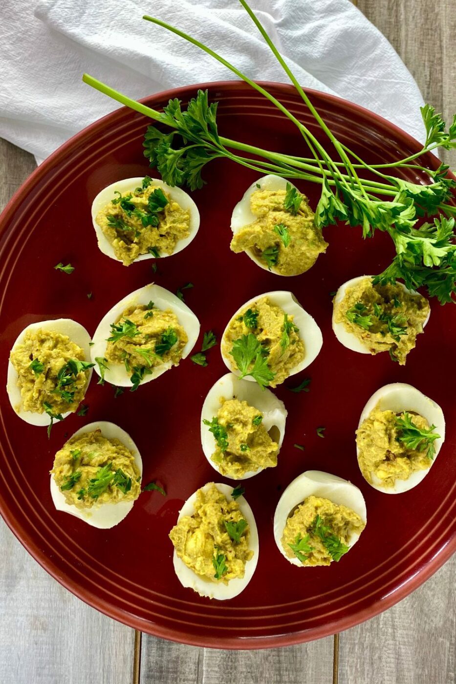 A platter of creamy green avocado deviled eggs garnished with paprika and chives.