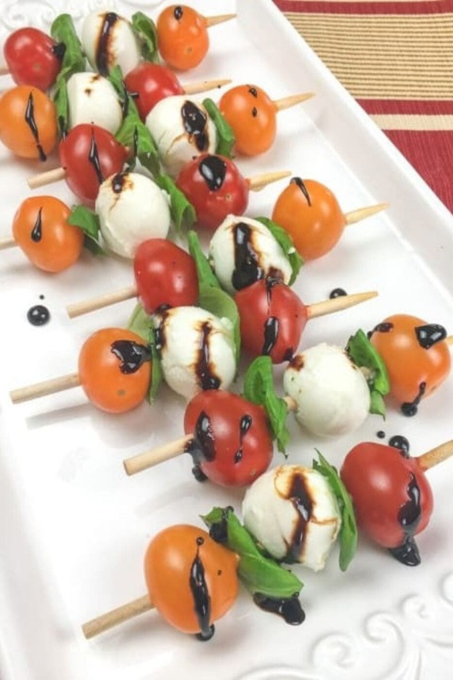 A platter of colorful Caprese salad skewers featuring cherry tomatoes, mozzarella balls, and fresh basil leaves, drizzled with balsamic glaze.