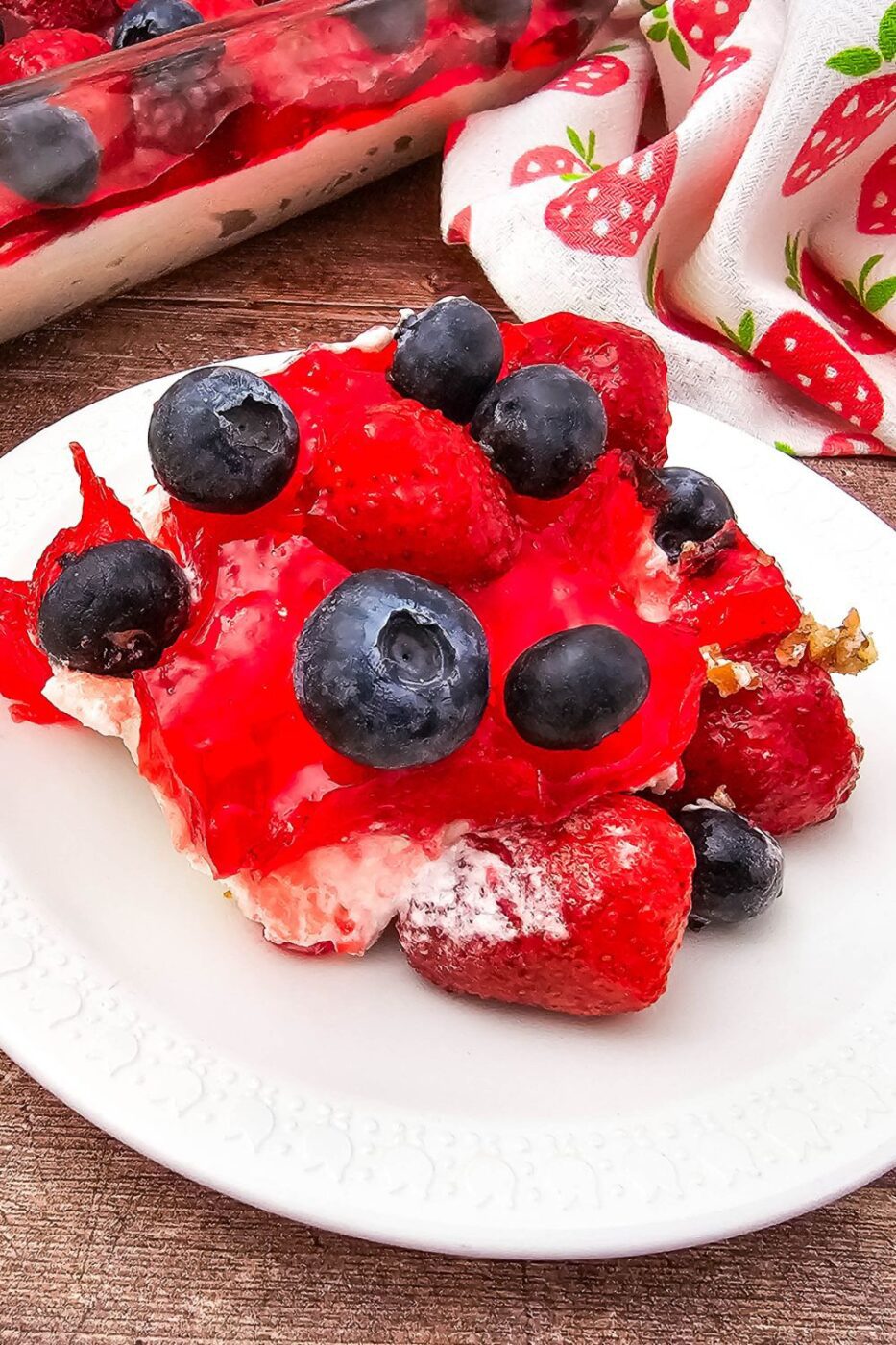 A vibrant, layered strawberry blueberry pretzel salad with a golden pretzel crust in a clear dish.