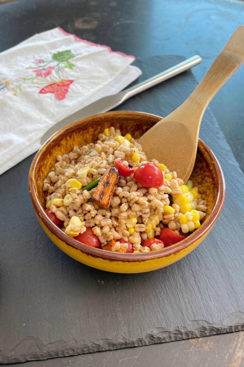 A colorful bowl of farro salad mixed with roasted vegetables like bell peppers, zucchini, and cherry tomatoes.