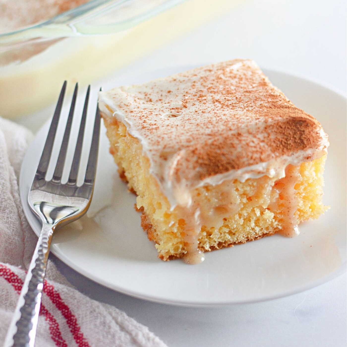 Recipe card featuring cinnamon roll poke cake slice with cinnamon dust and fork.
