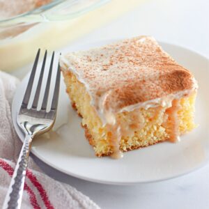 Recipe card featuring cinnamon roll poke cake slice with cinnamon dust and fork.