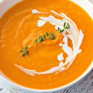 Creamy butternut squash soup recipe card image with swirl of cream and herbs.