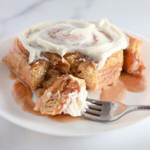 Single TikTok cinnamon roll with frosting on a white plate and fork.