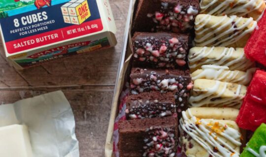 Challenge Dairy butter cubes next to a cookie tin with three kinds of festive, square cookies.