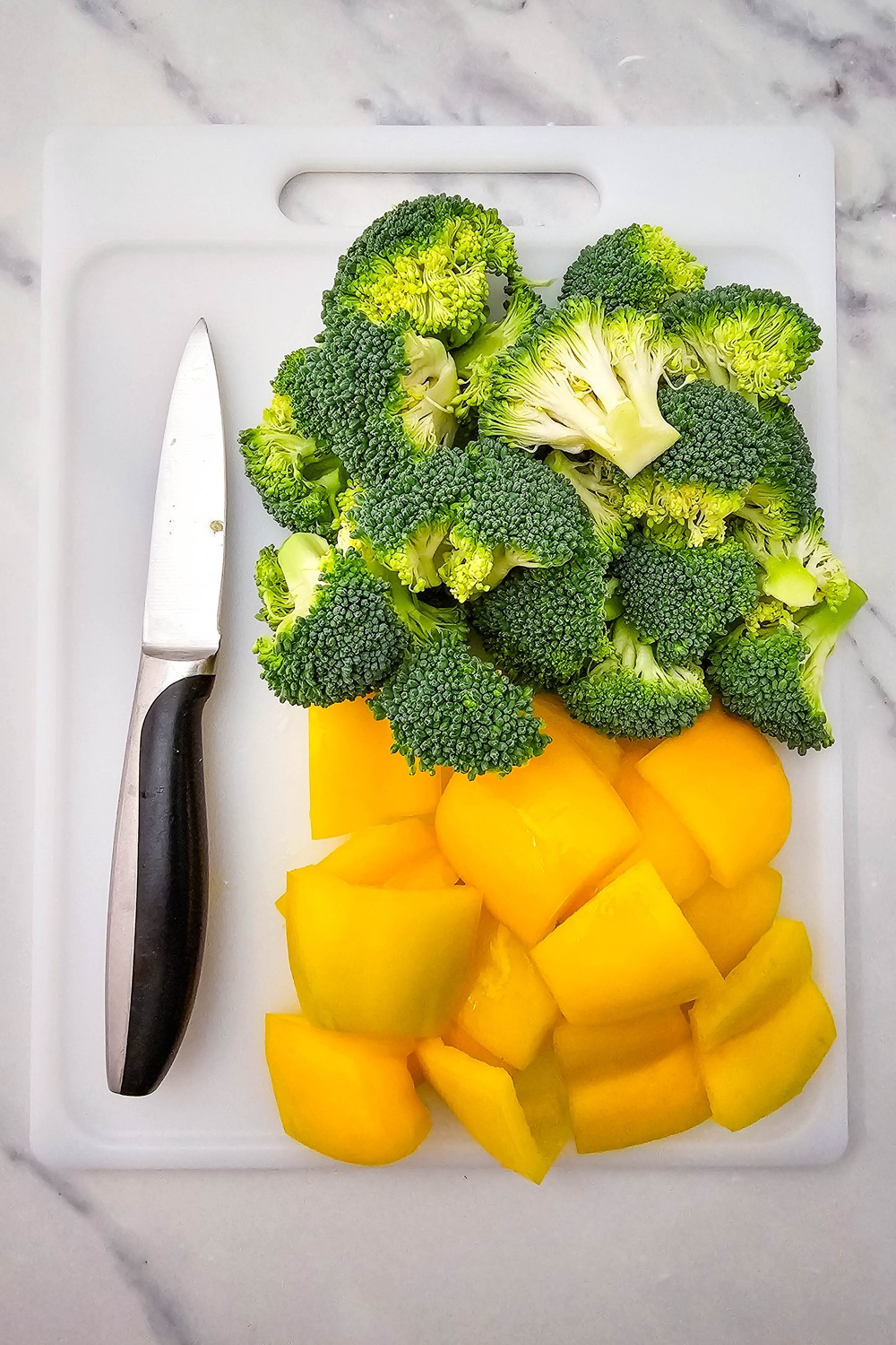 Chopped broccoli florets and yellow bell pepper pieces on a cutting board