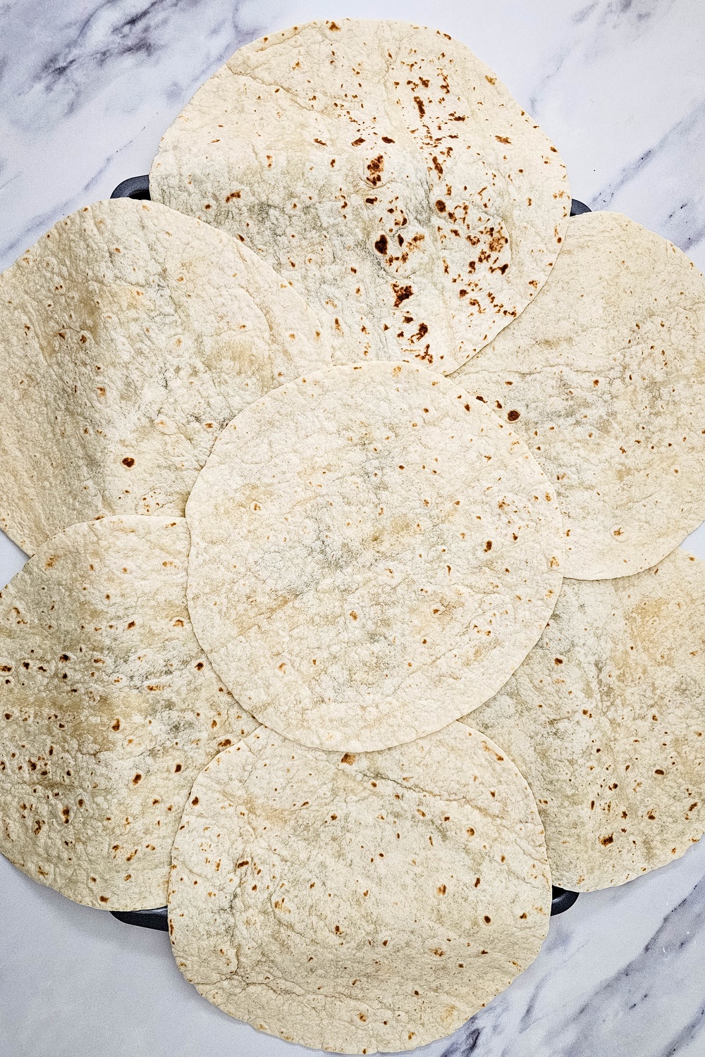 Flour tortillas arranged overlapping on a sheet pan