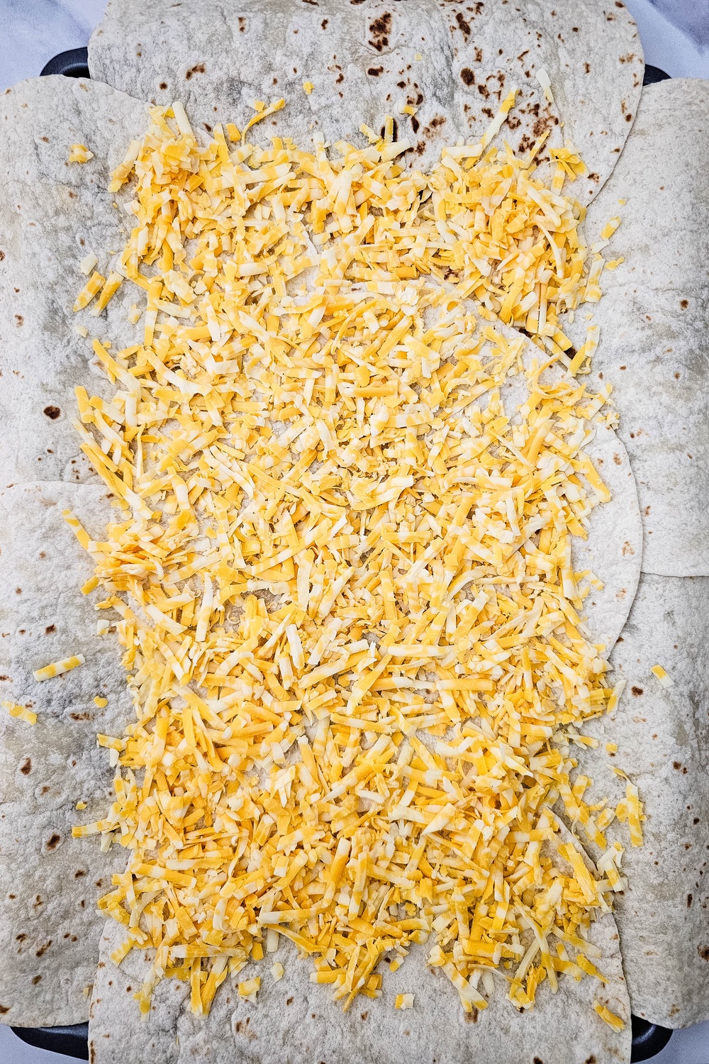 Shredded colby jack cheese sprinkled over tortillas on the sheet pan
