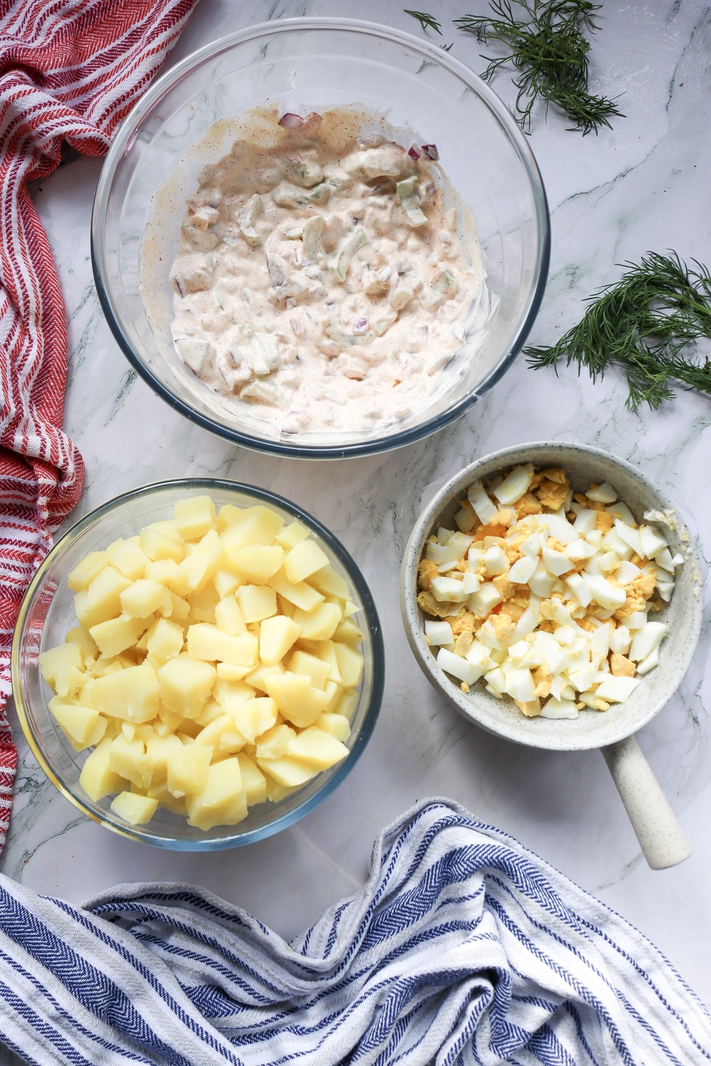 Mise en place for combining 4th of July potato salad: dressing, diced potatoes, and chopped hard-boiled eggs