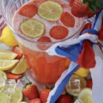 Top-down view of a glass pitcher of 4th of July strawberry lemonade with floating lemon wheels and fresh strawberries