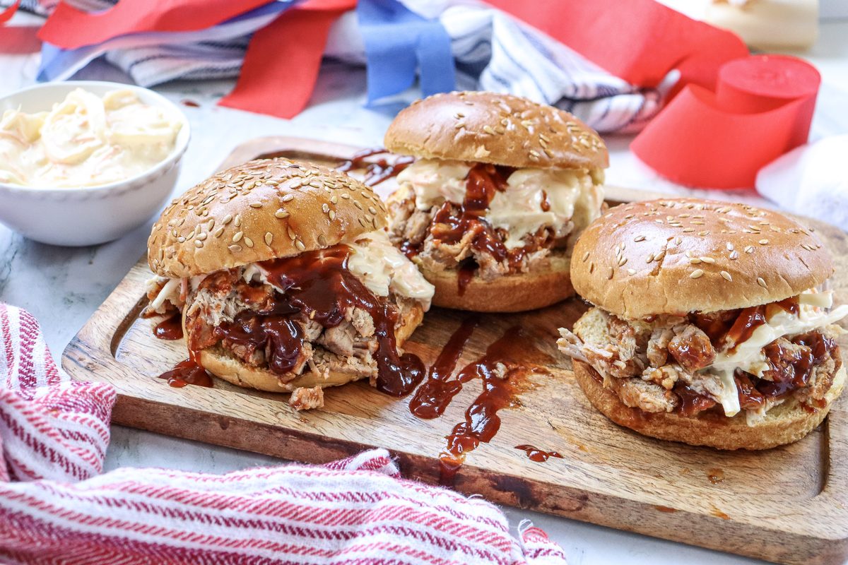 BBQ pulled pork sandwiches on a wooden board with a 4th of July red, white, and blue background, perfect for a summer cookout party.