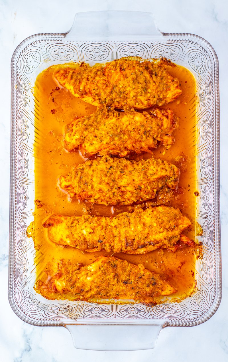 Spooning butter parmesan mixture over seasoned chicken on a baking sheet