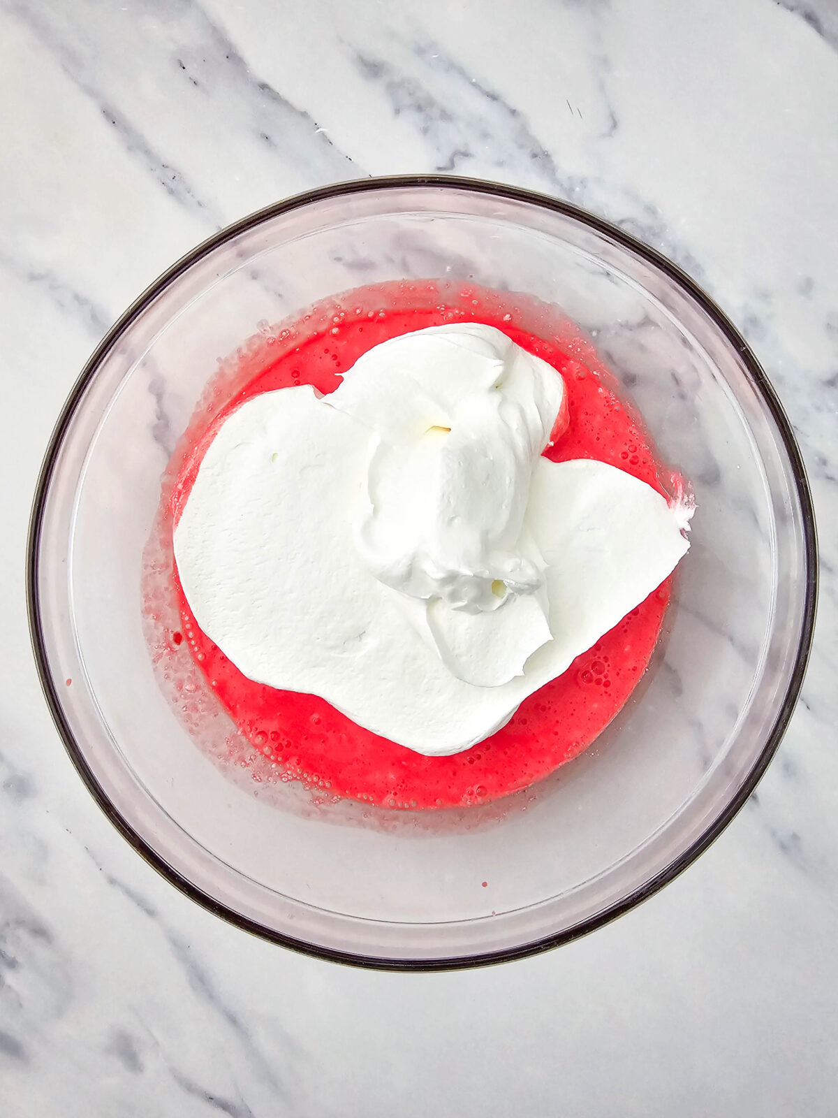 Cool Whip dolloped on top of the pink gelatin and cottage cheese mixture