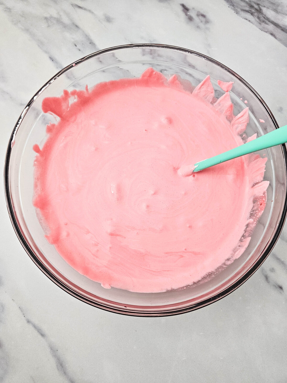 Smooth, even pink fluff mixture in a glass bowl with a teal spatula