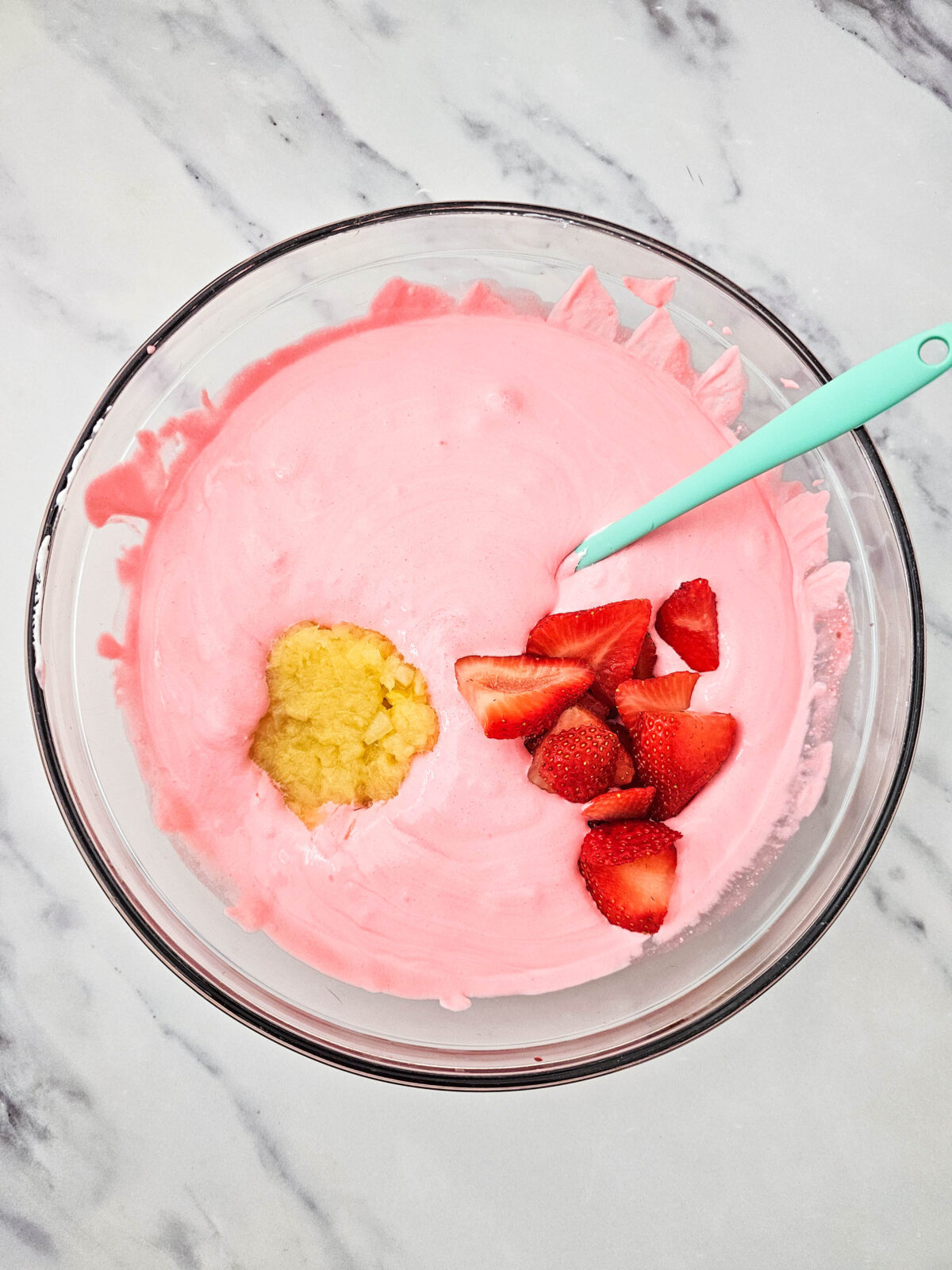 Drained crushed pineapple and sliced strawberries added to the pink fluff mixture, ready to be folded in