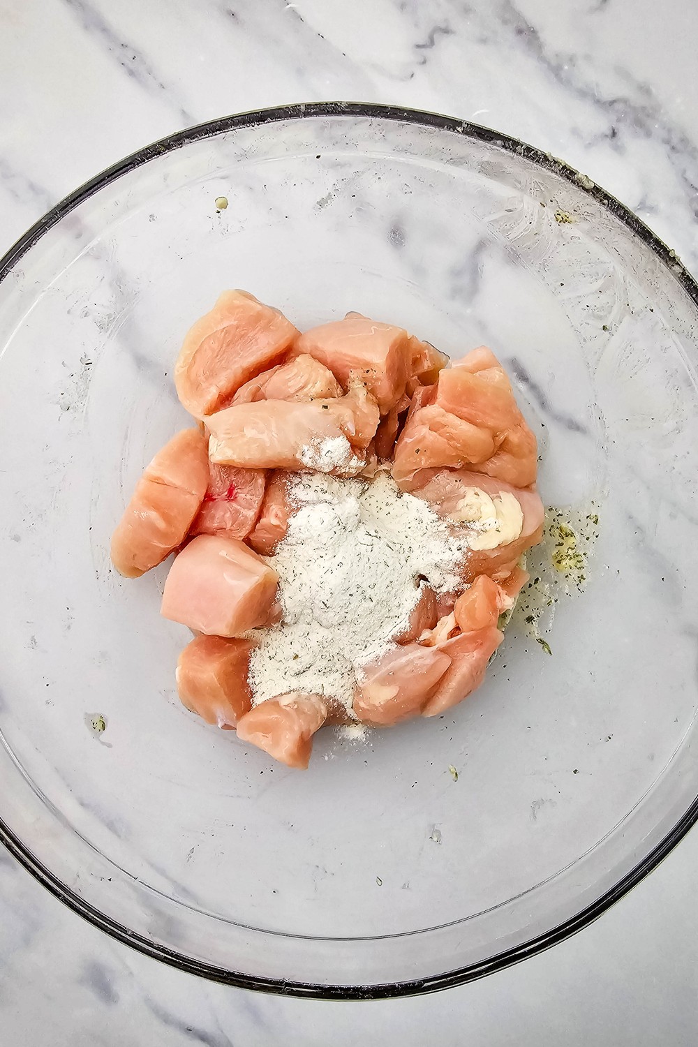 Cubed chicken breast in a glass bowl with a dry ranch seasoning packet poured on top.