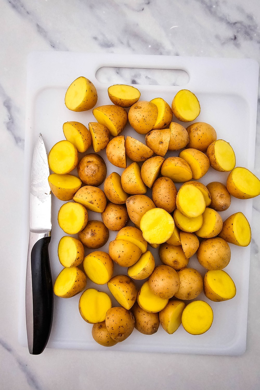 Baby potatoes halved on a white cutting board, ready for roasting.