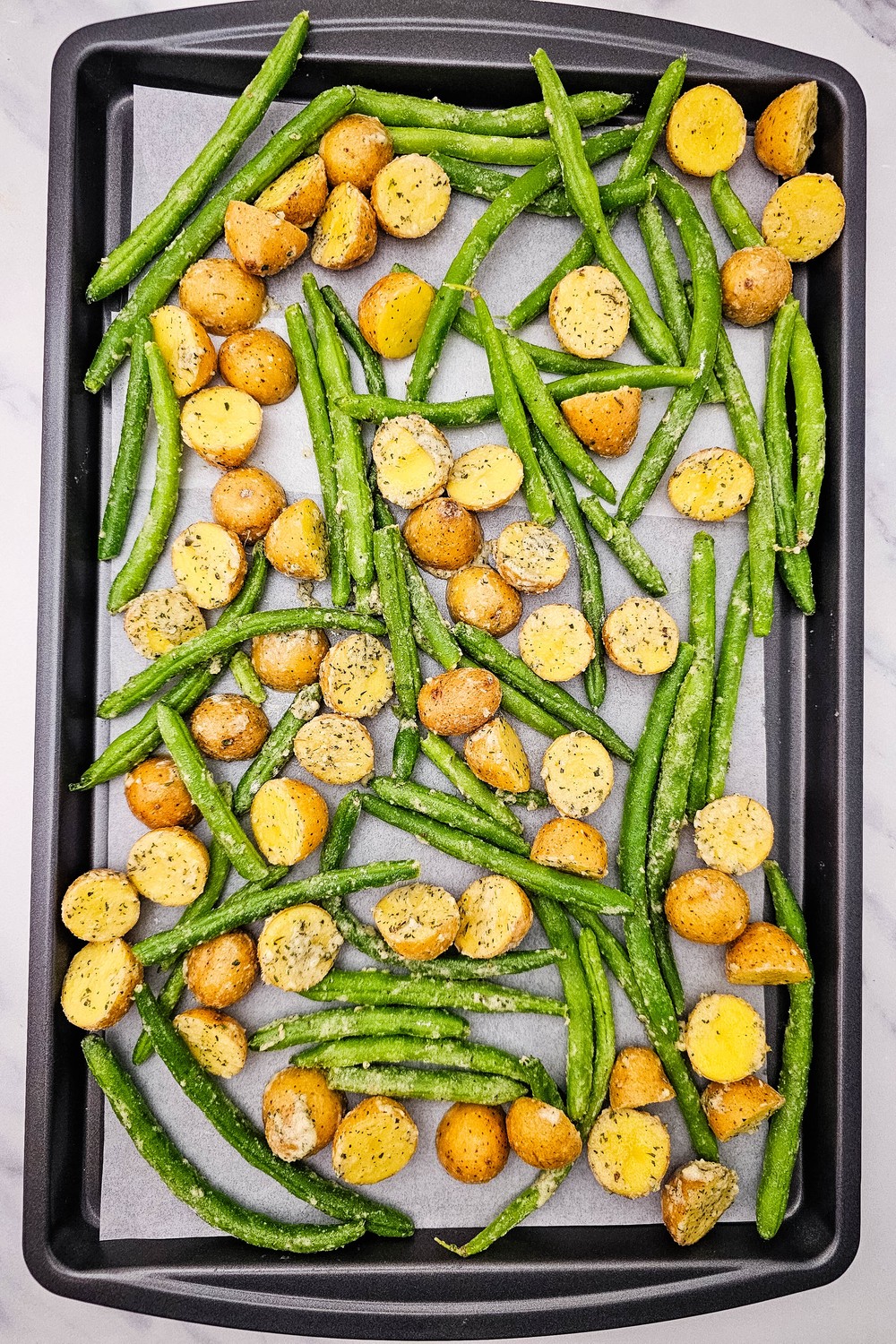 Ranch-coated potatoes and green beans spread out on a parchment-lined sheet pan.